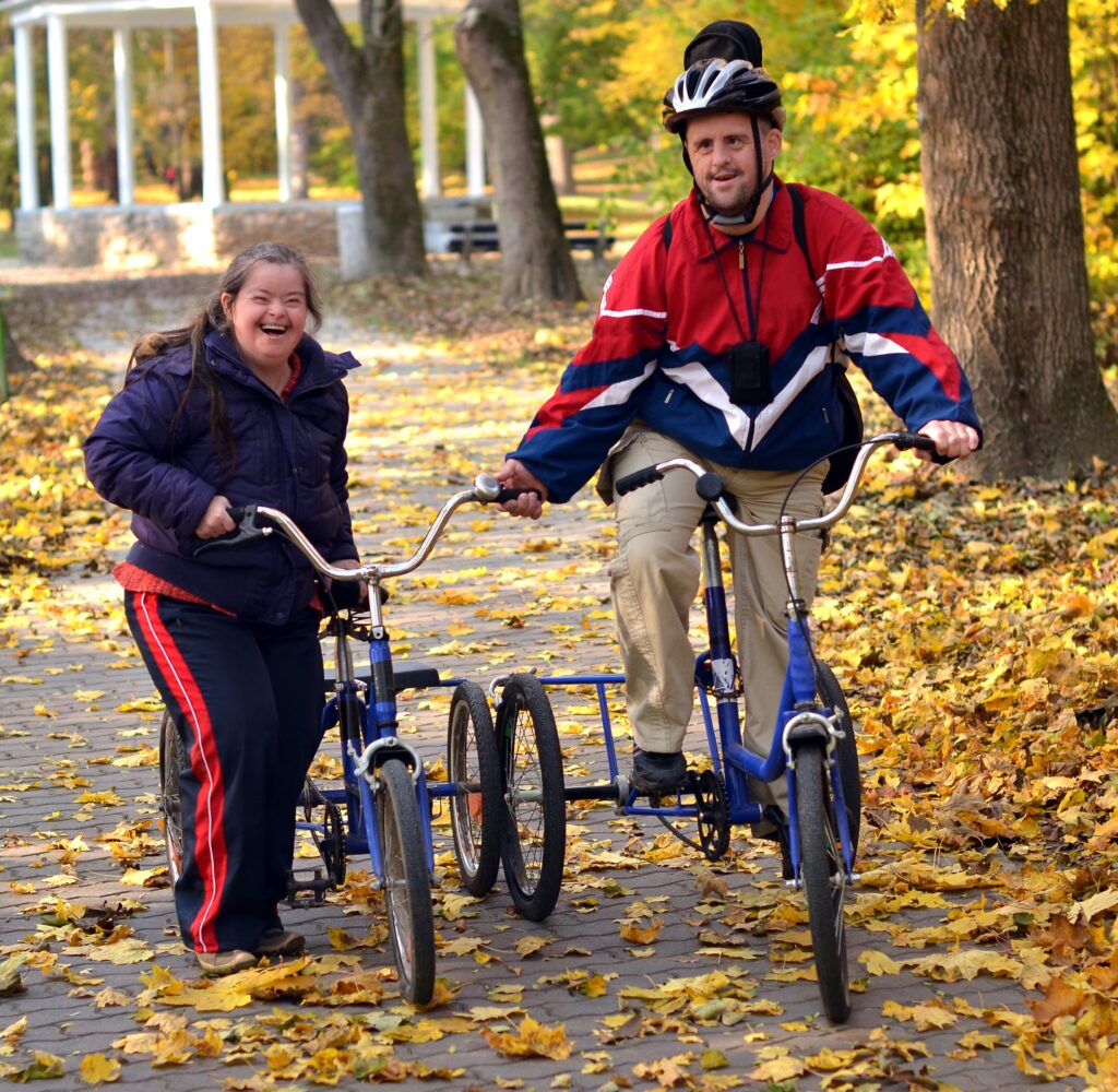 Two individuals enjoying an autumn bike ride in the park — supported living enabling active, fulfilling lives